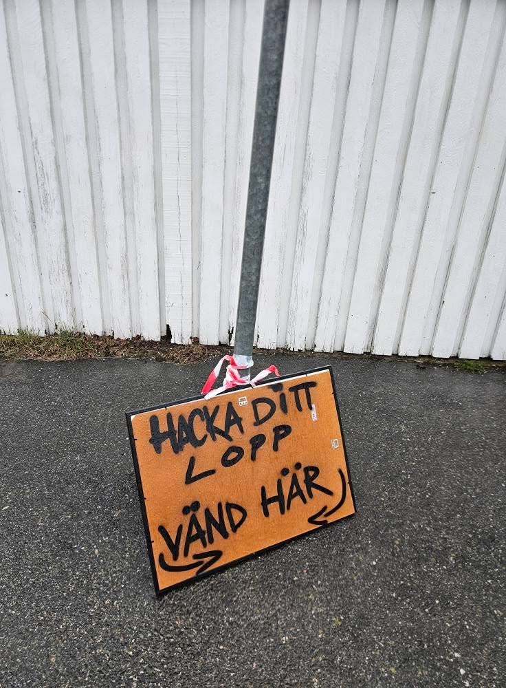 Handskriven skylt i kartong: HACKA DITT LOPP VÄND HÄR med pilar, tejpad mot lyktstolpe under HackaDittLivLoppet 2025 i Göteborg